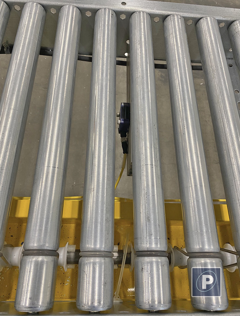 Close up of a photo-eye sensor integrated directly between the metal conveyor rollers for automated PLC handshake with the Pro 1100